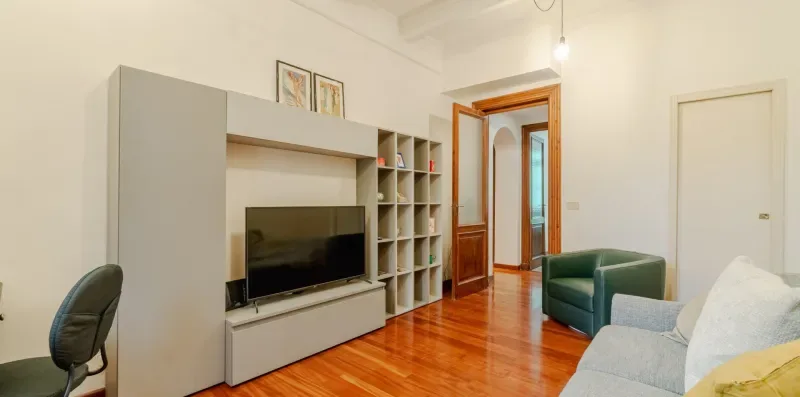 Una sala de estar luminosa con televisor, estanterías y asientos.