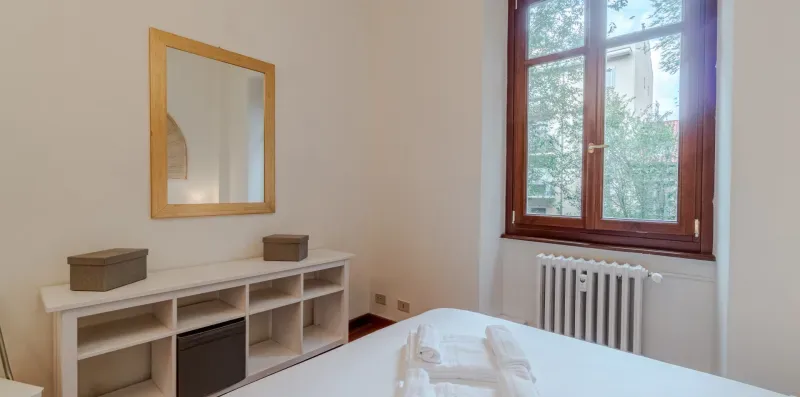 Un dormitorio con una cama, un mueble bajo con estantes y una ventana grande.