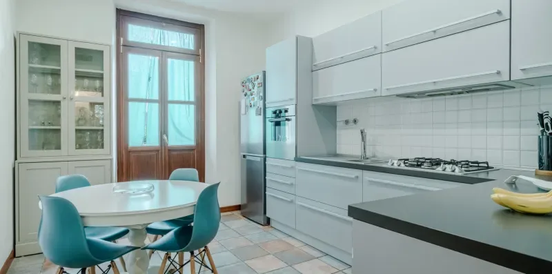 Una cocina moderna y luminosa con gabinetes blancos, una mesa de comedor y asientos azules.
