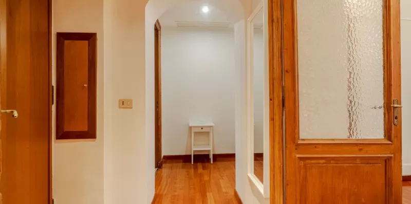Un pasillo con puertas de madera y un pequeño taburete al fondo.