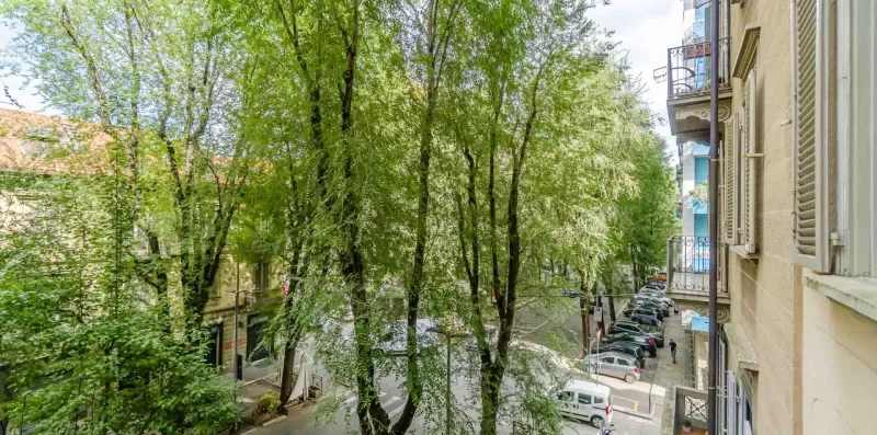 Vista de una calle arbolada desde arriba, con autos estacionados y edificios de apartamentos.