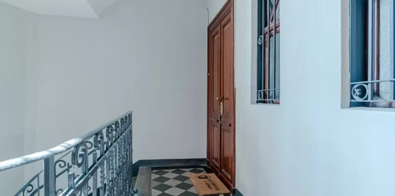 Un pasillo interior con suelo estampado, una puerta de madera y barandillas metálicas.