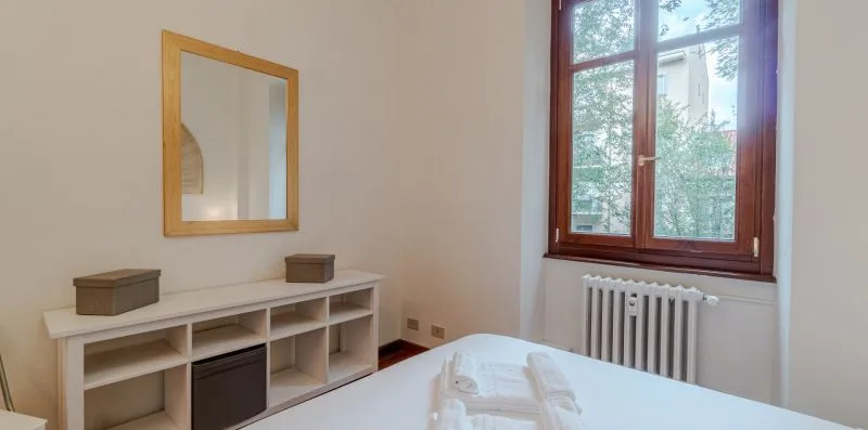 Un dormitorio con una cama, un mueble bajo con estantes y una ventana.