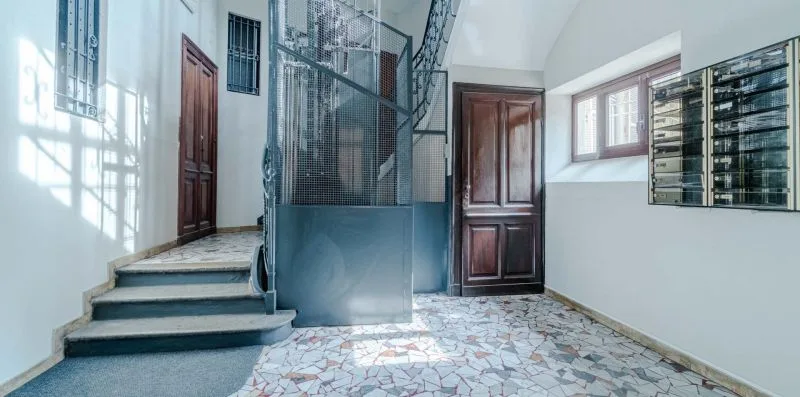 Un descansillo interior con escalones de piedra, una reja metálica y puertas de madera.