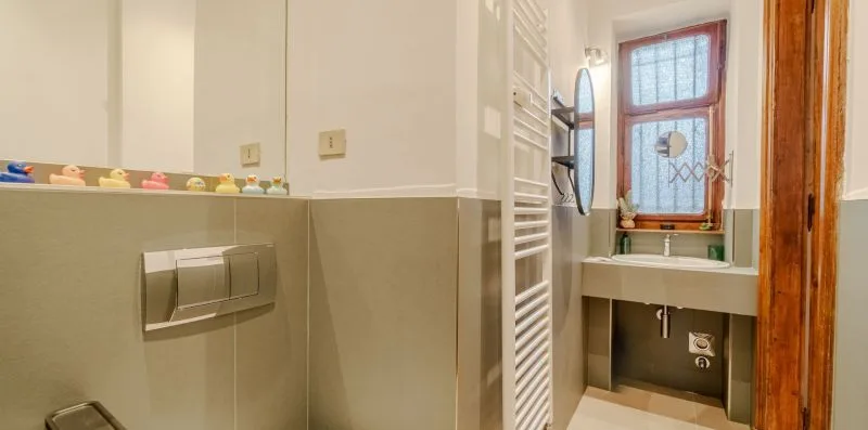 Un baño con un lavabo de pared debajo de una ventana.