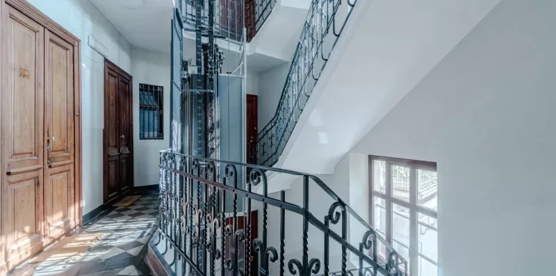 Una escalera interior con barandillas ornamentadas, puertas de madera y ventanas grandes.