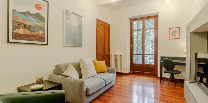 Una sala luminosa con sofá, cuadros enmarcados y ventanas altas.
