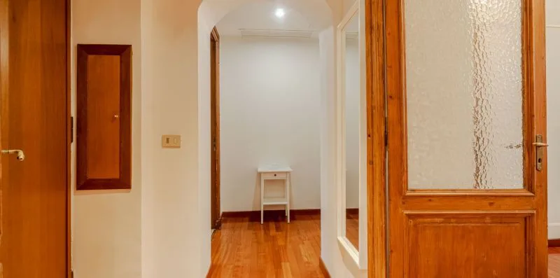 Un pasillo con puertas de madera y una mesita al fondo.