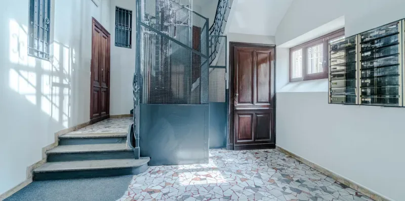 Una escalera interior con barandilla metálica y suelo de baldosas estampadas.