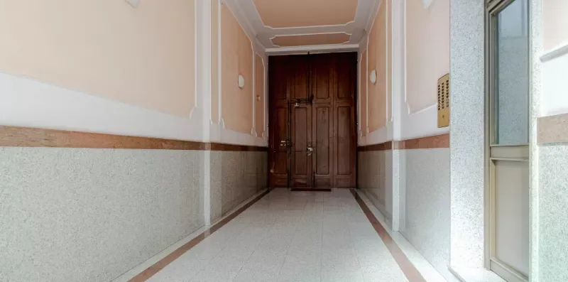 Un pasillo estrecho conduce a una puerta de madera oscura, con una ventana a un lado.