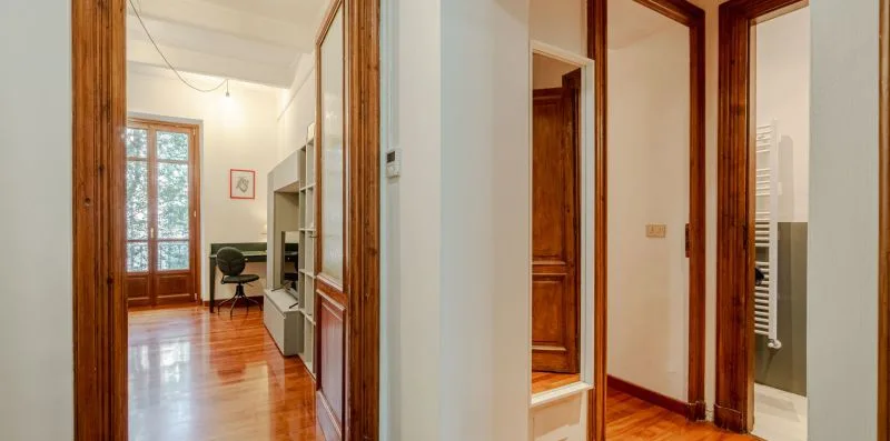 Un pasillo luminoso se abre hacia una habitación con suelo de madera y un escritorio.