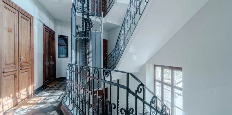 Una escalera interior con barandillas ornamentadas, puertas de madera y ventanas.