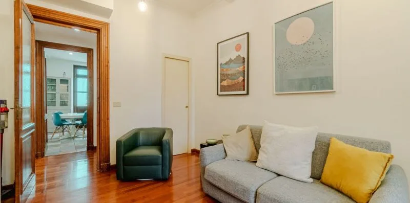 Una sala de estar con un sofá gris, un sillón verde y cuadros en la pared.