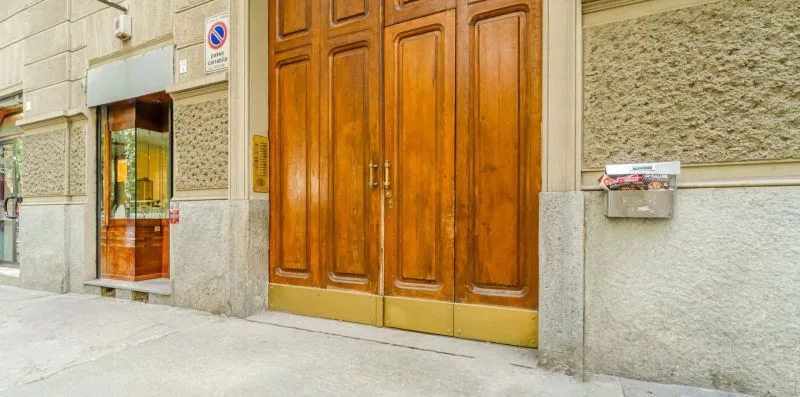 Entrada de un edificio a la calle, con una gran puerta de madera y una ventana cercana.