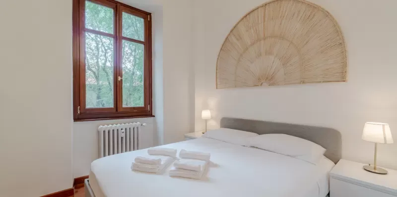 Un dormitorio con una cama bien tendida bajo un adorno de pared en forma de abanico.