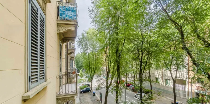Una calle arbolada pasa junto a un edificio claro con balcones.