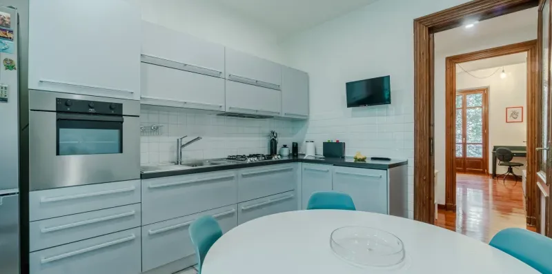 Una cocina moderna con gabinetes blancos, electrodomésticos empotrados y una mesa de comedor.