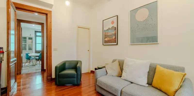 Una sala de estar con un sofá gris, cojines de colores y cuadros en la pared.