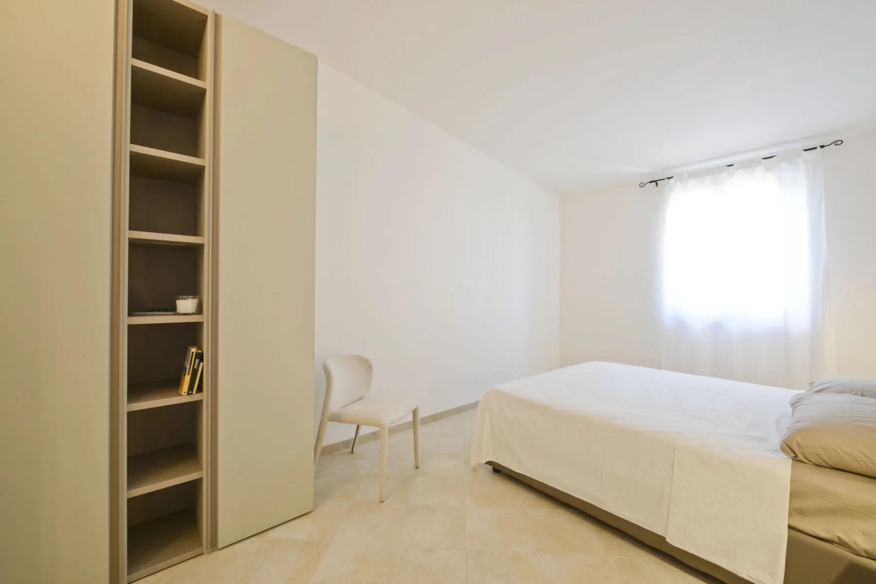 A bright bedroom with a bed, a chair, and built-in shelving.