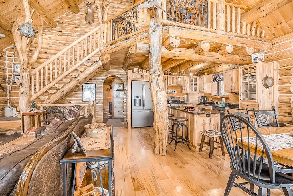 Interior de cabaña revestido de madera, con cocina y comedor abiertos bajo un altillo.