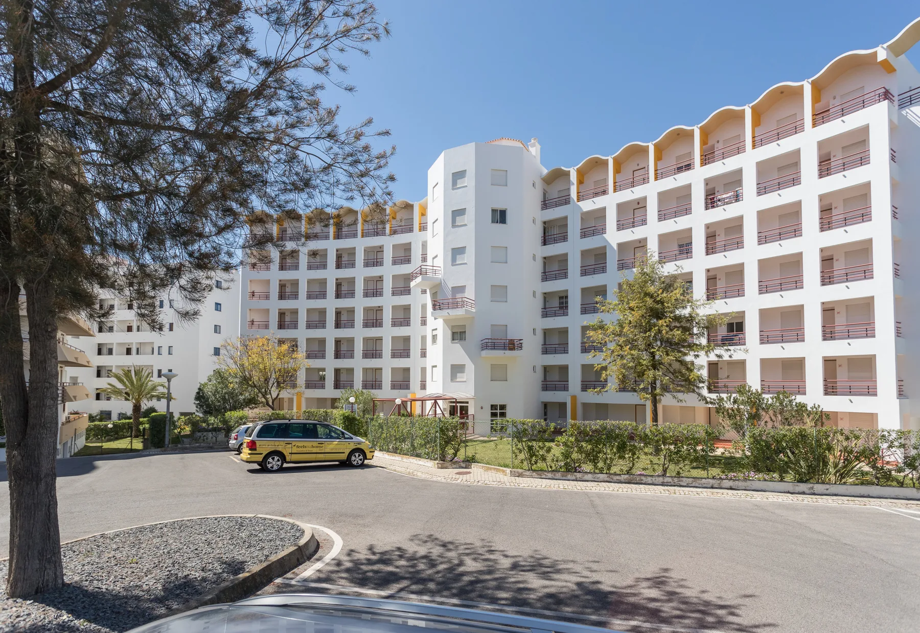 Un edificio de apartamentos se alza junto a una carretera curva y zonas ajardinadas.