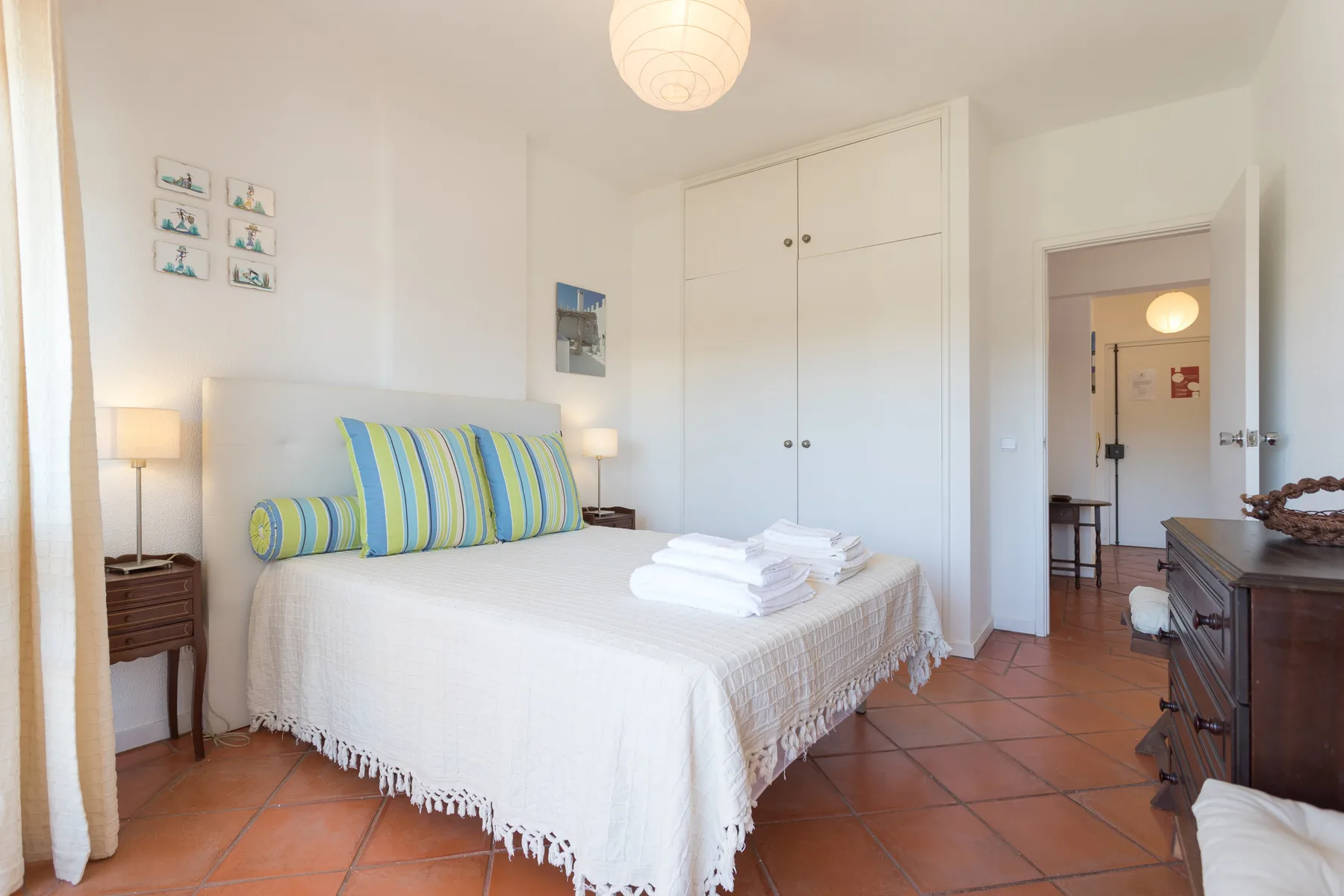 Un dormitorio luminoso con una cama, cojines a rayas y armarios empotrados.