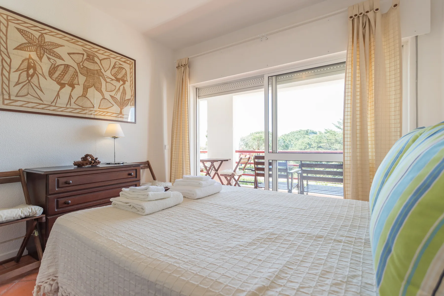 Un dormitorio luminoso con una cama bien hecha junto a puertas correderas de vidrio.