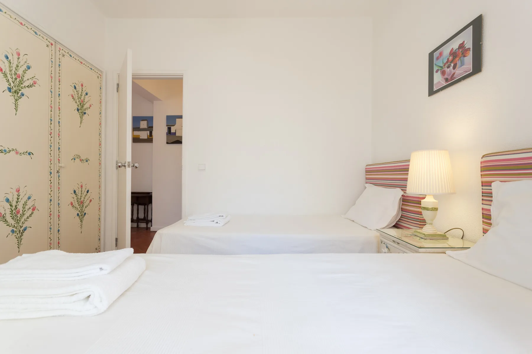 A bedroom with two beds, a bedside lamp, and floral-patterned closet doors.