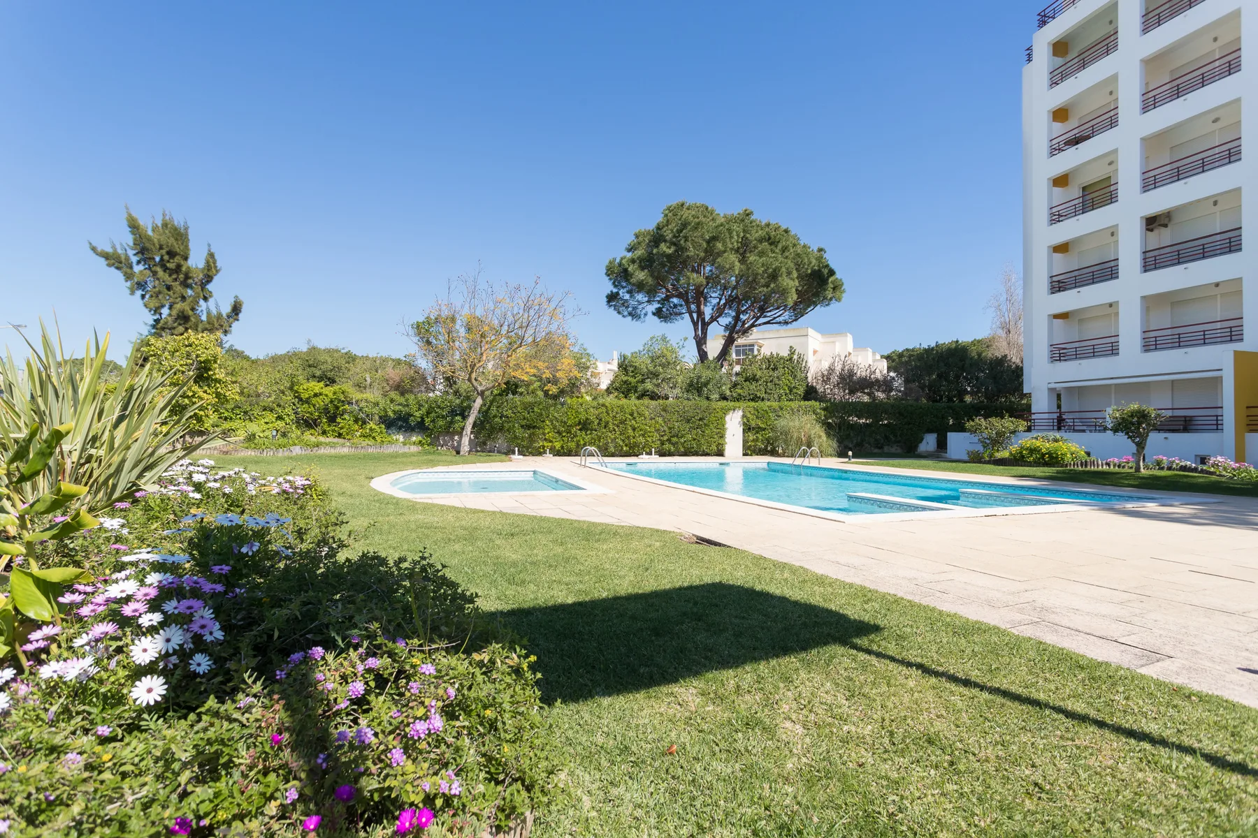 Una piscina exterior junto a un césped y un edificio de apartamentos.