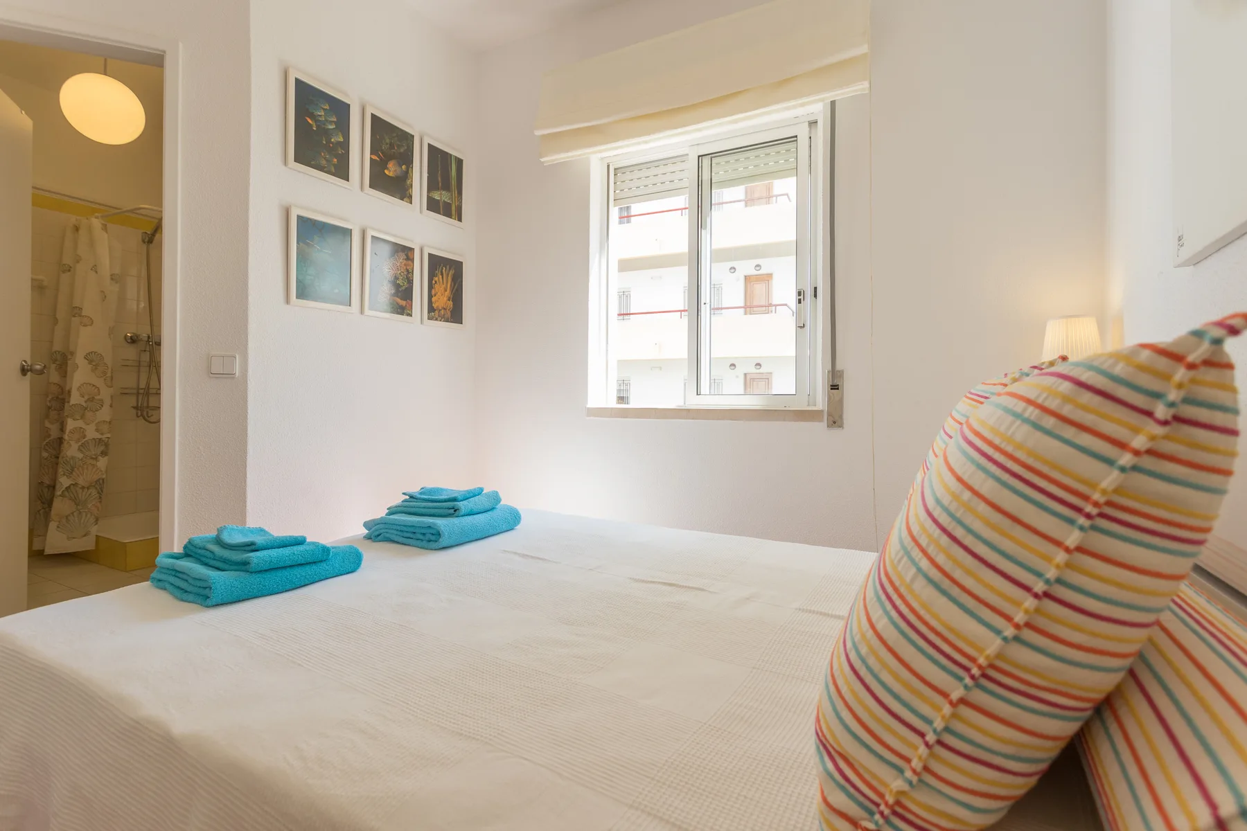 A bright bedroom with a bed, folded towels, and a window.
