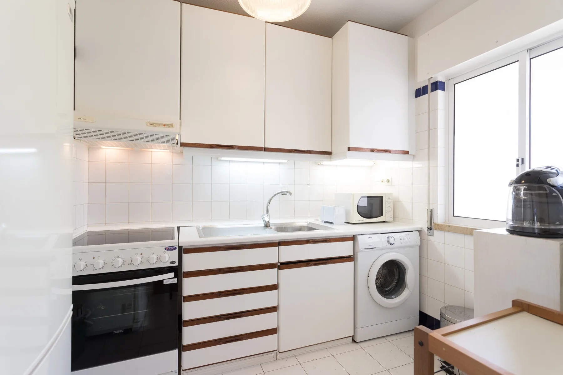 Una cocina luminosa con armarios blancos, un horno y una lavadora.