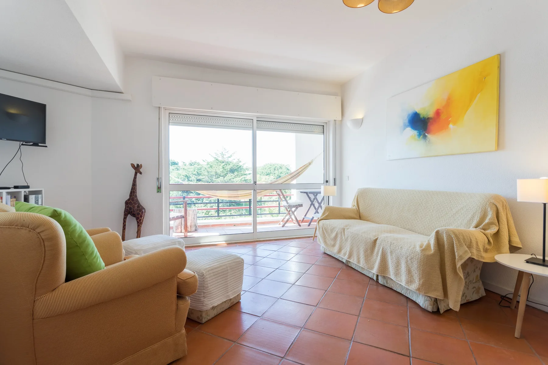 Sala de estar con asientos, un televisor y una amplia puerta acristalada que da a un balcón.