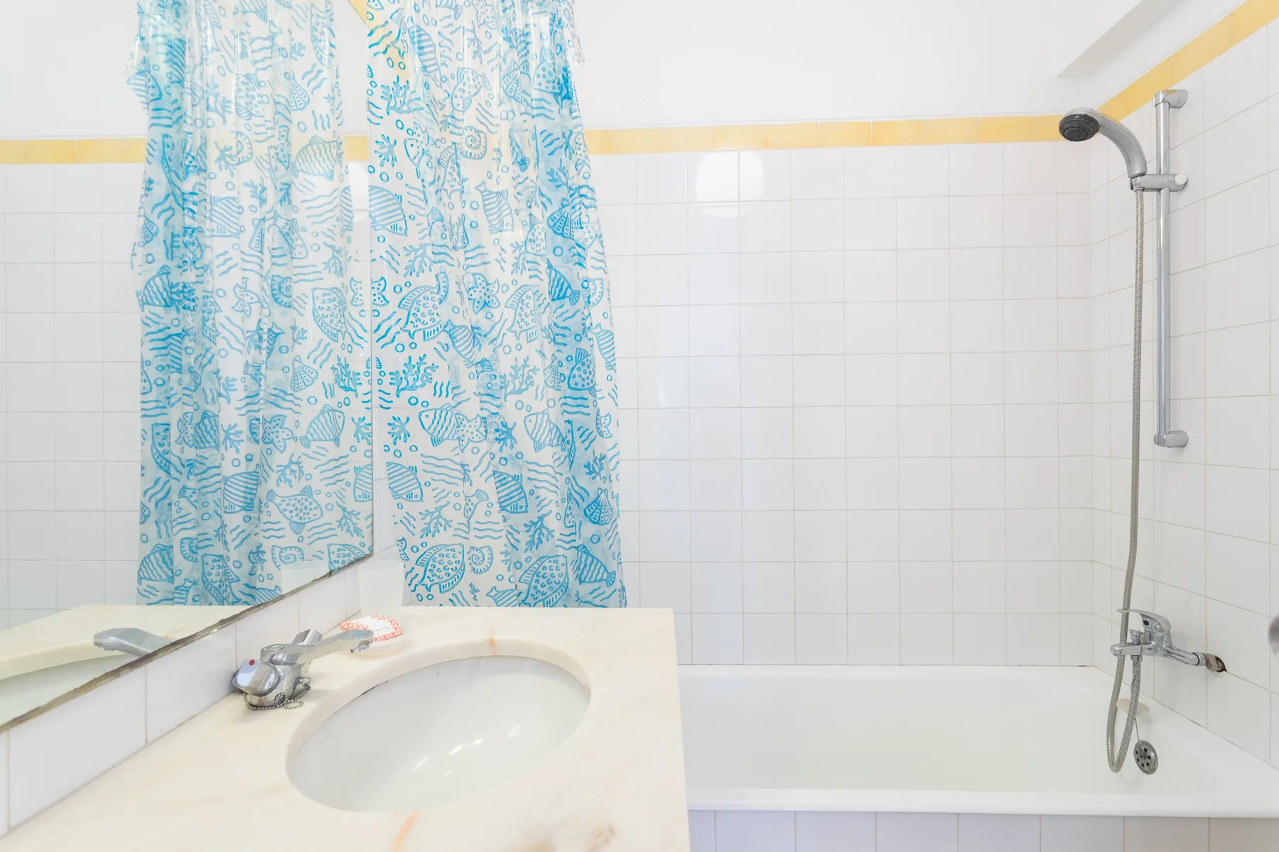 Un baño con bañera, ducha, lavabo y cortina azul estampada.