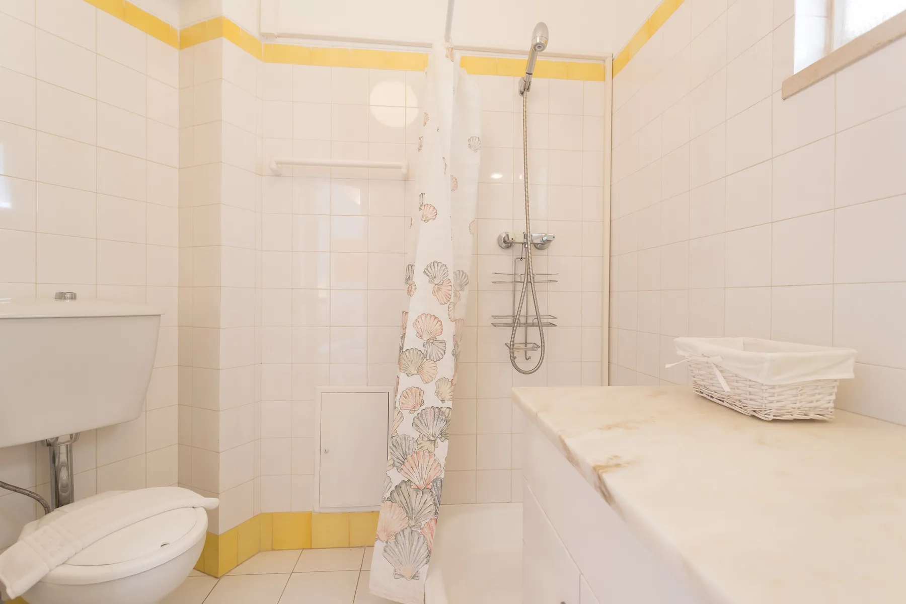 Un baño con azulejos, ducha, inodoro y encimera.