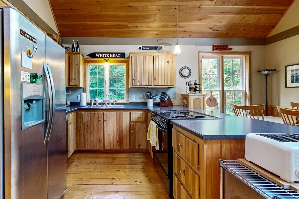 A wood-paneled kitchen with a central island and windows overlooking trees.