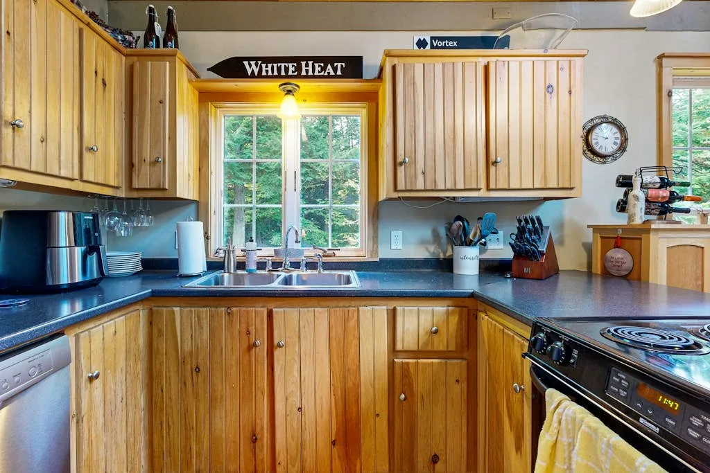 Una cocina con gabinetes de madera, fregadero bajo la ventana y estufa.