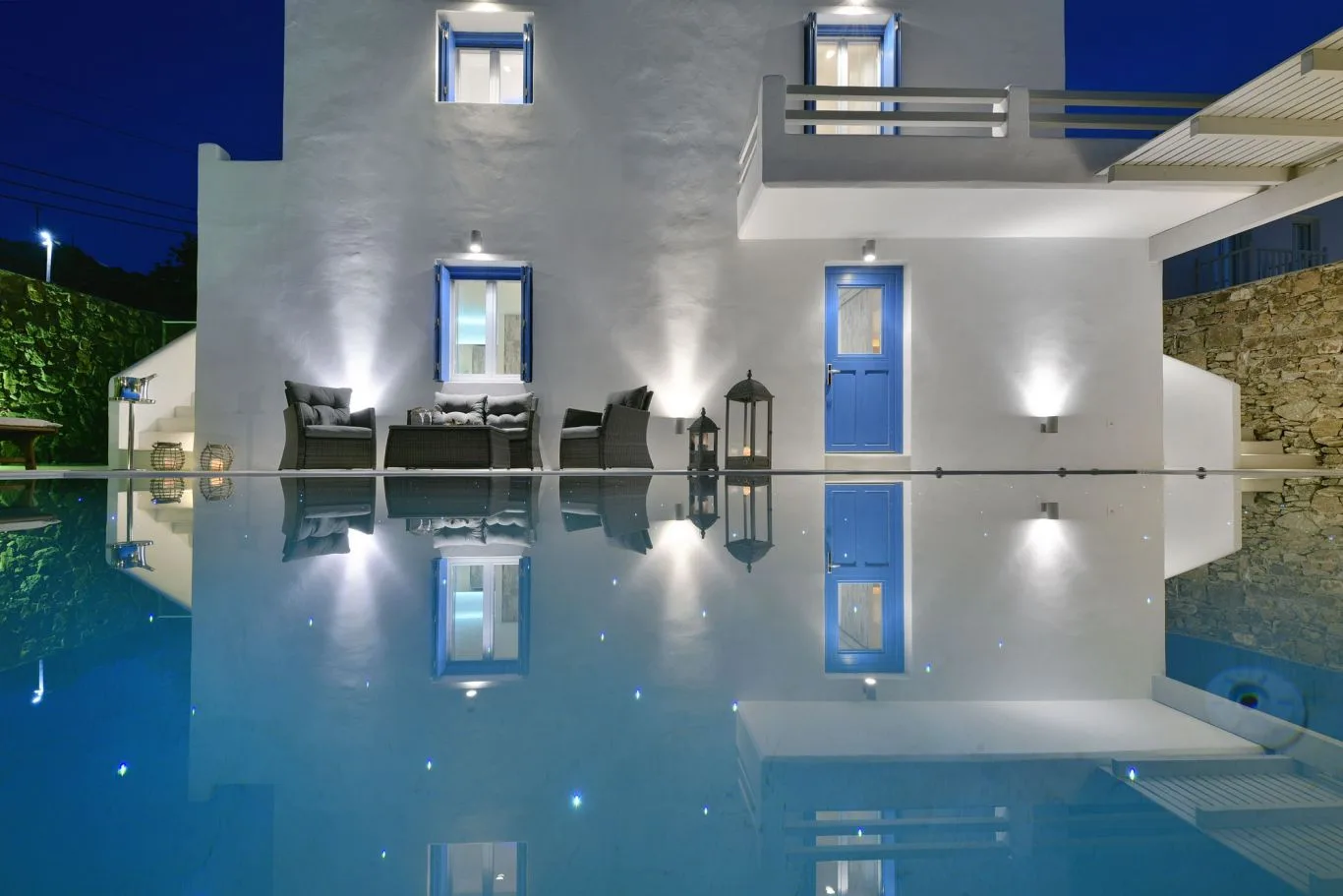 A white villa with blue doors stands beside a lit swimming pool at night.