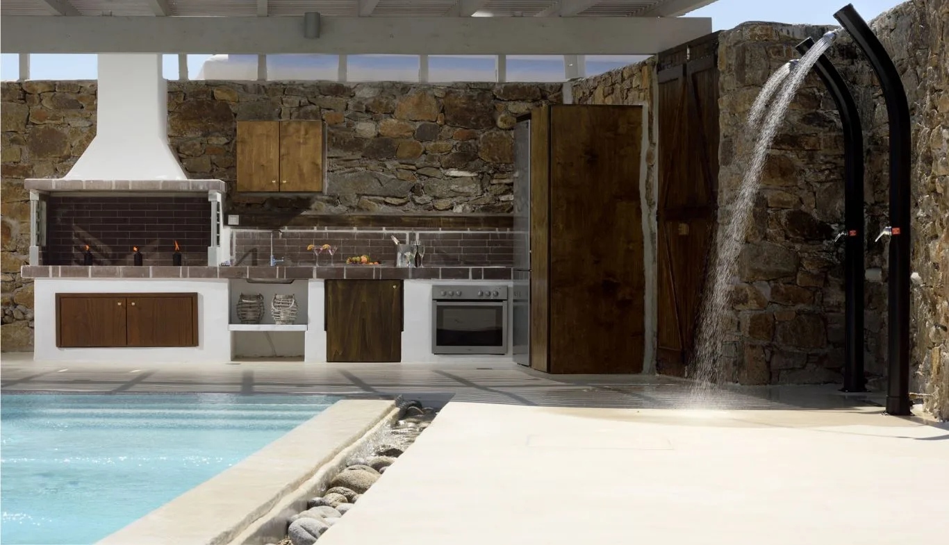 An outdoor pool beside a stone-walled kitchen and shower.