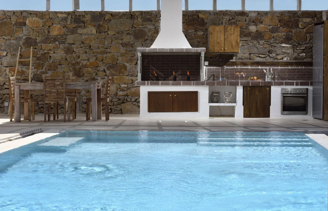 An outdoor pool in front of a stone wall and cooking area.