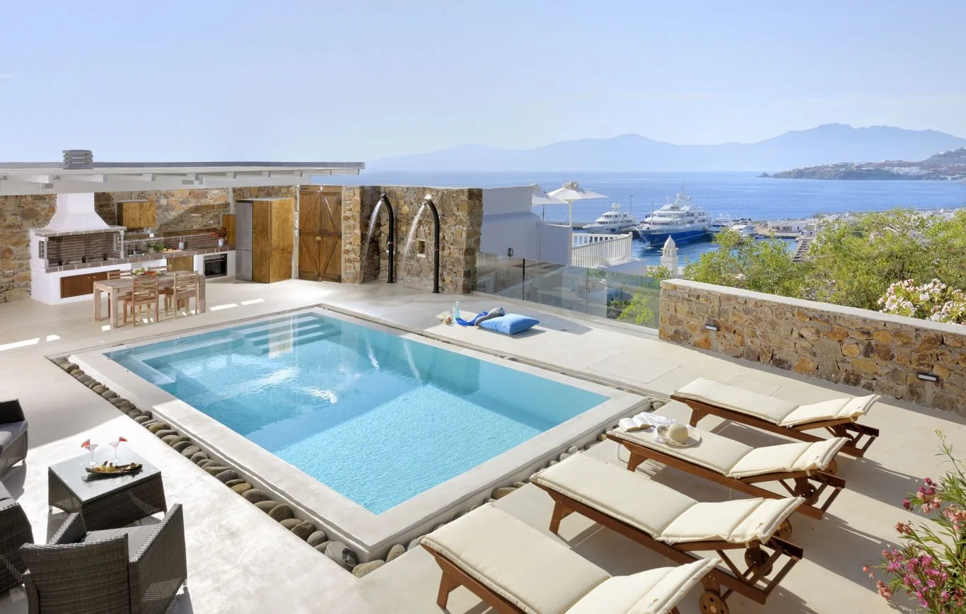 A swimming pool and sun loungers overlook the sea and marina.