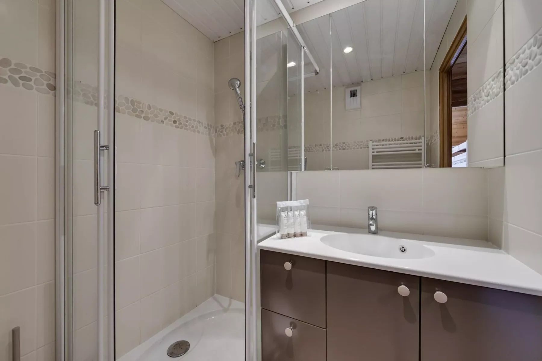 A tiled bathroom with a glass shower and a sink beneath a large mirror.