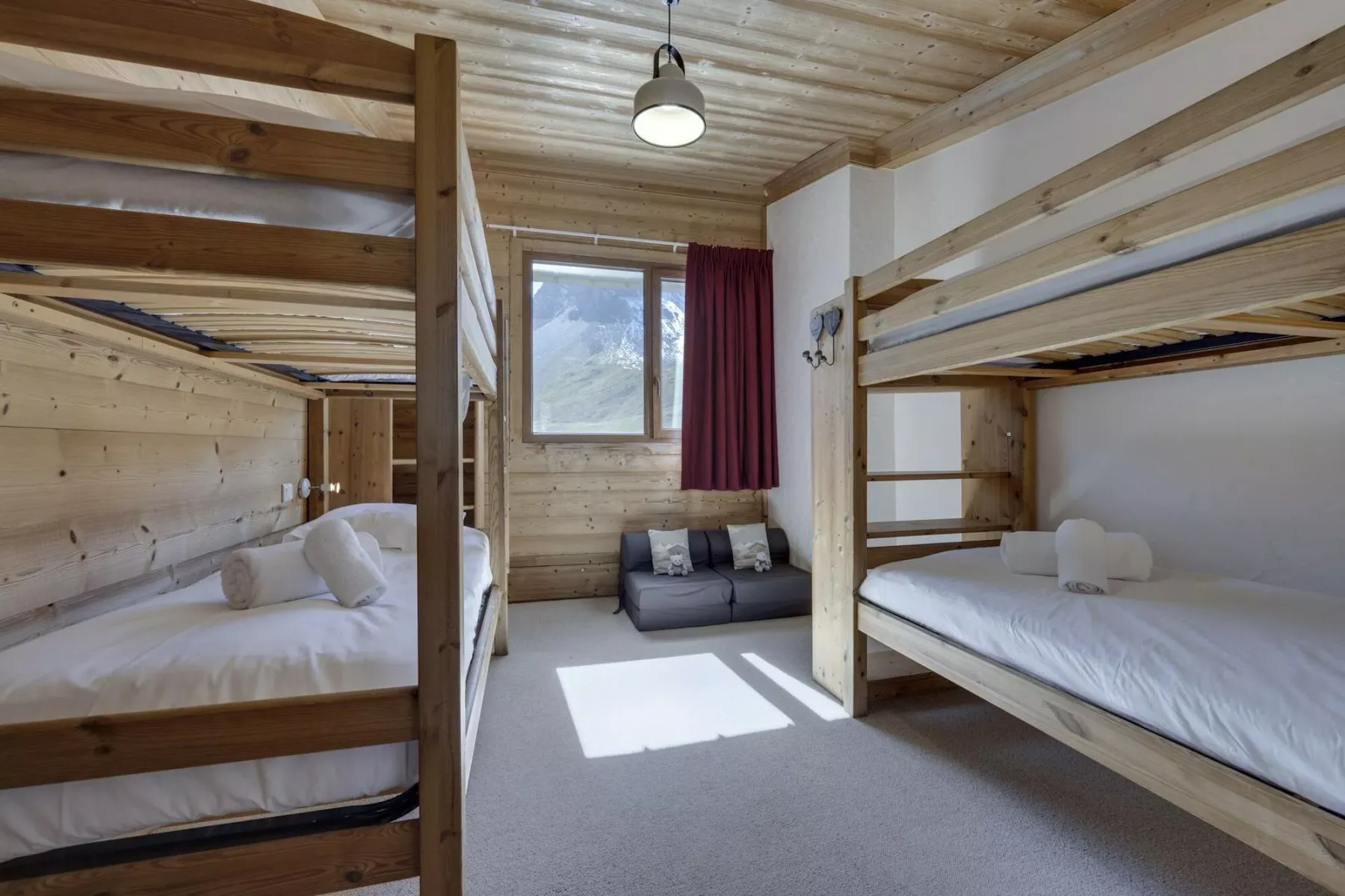 A wood-paneled bedroom with bunk beds and a small seating area beneath the window.