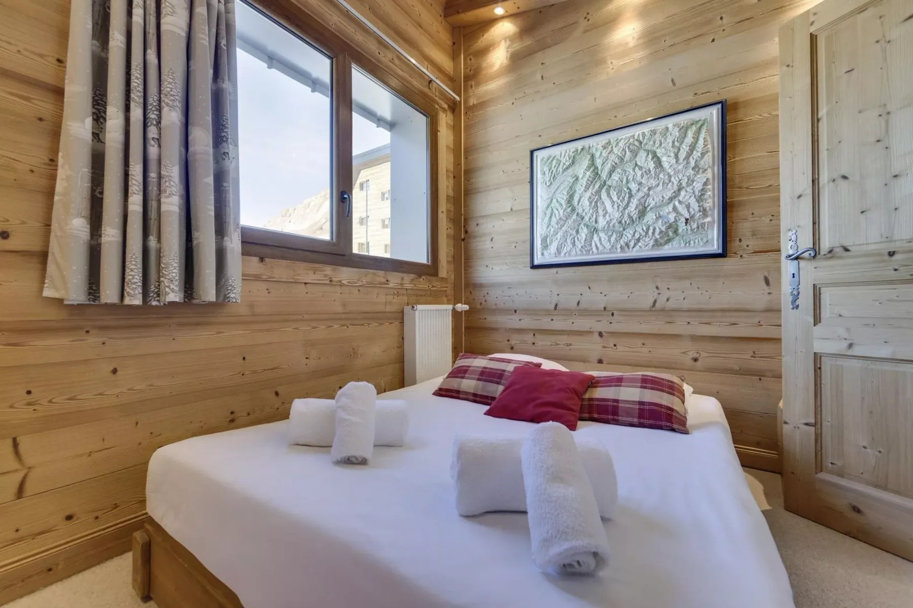 A bedroom with a bed, patterned pillows, and wood-paneled walls.