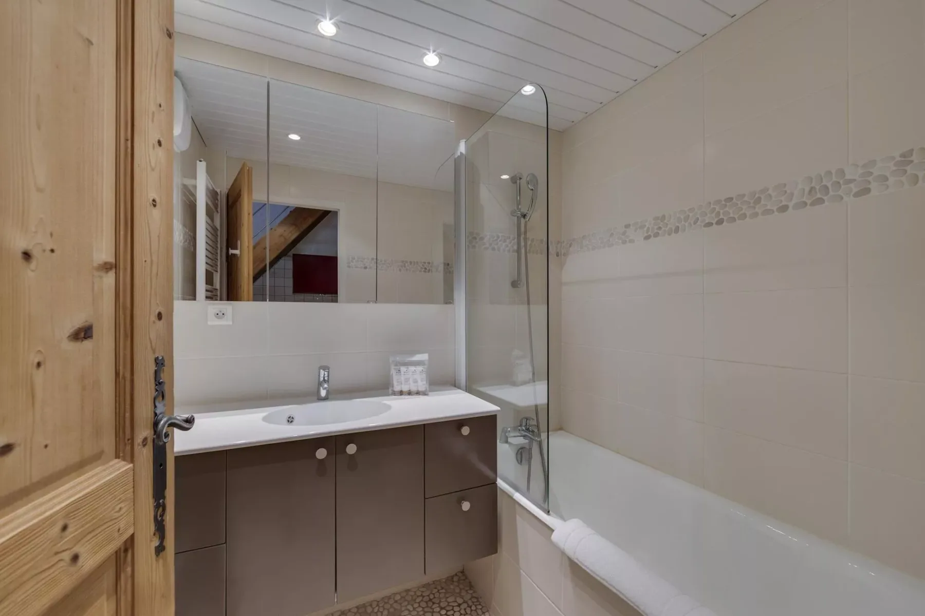 A bathroom with a bathtub, glass shower screen, and vanity.