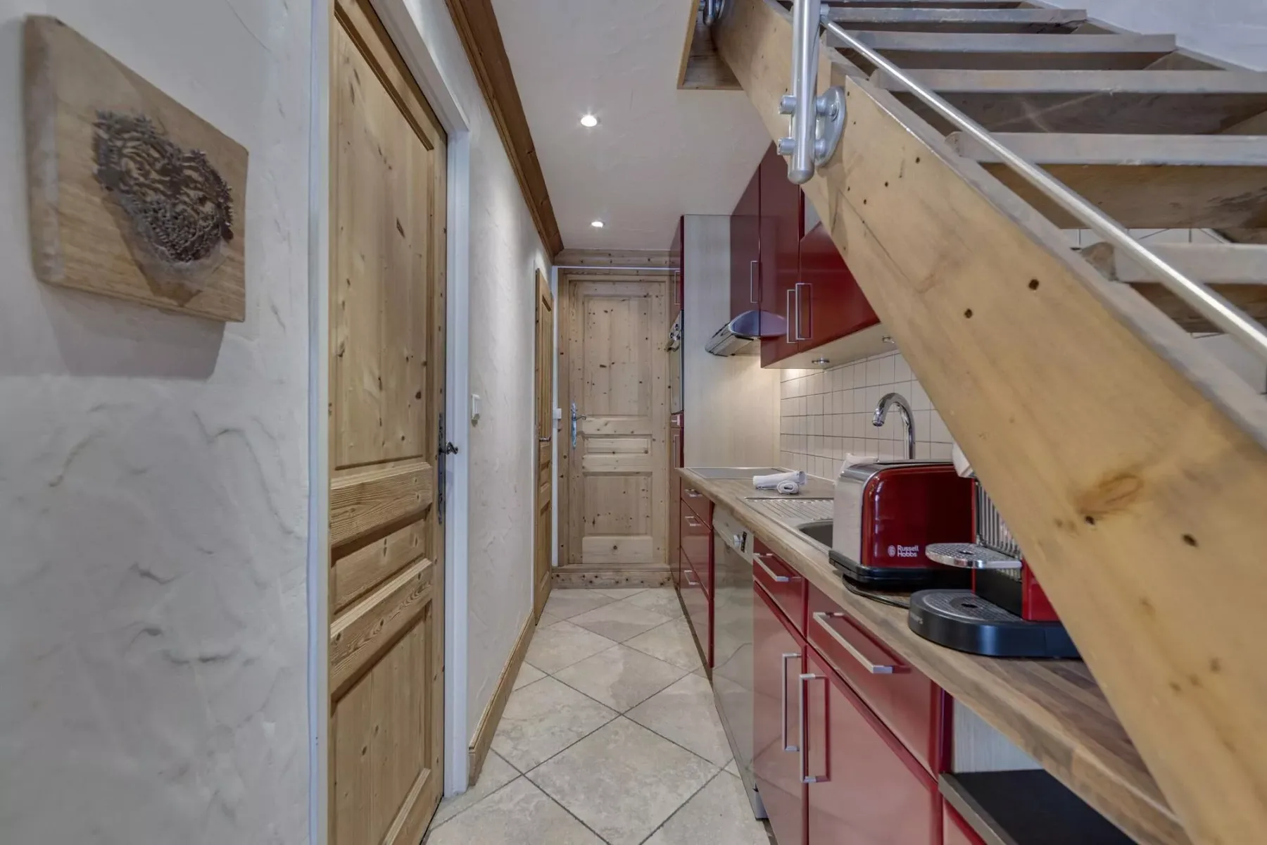 A narrow kitchen hallway with red cabinets and a wooden staircase.