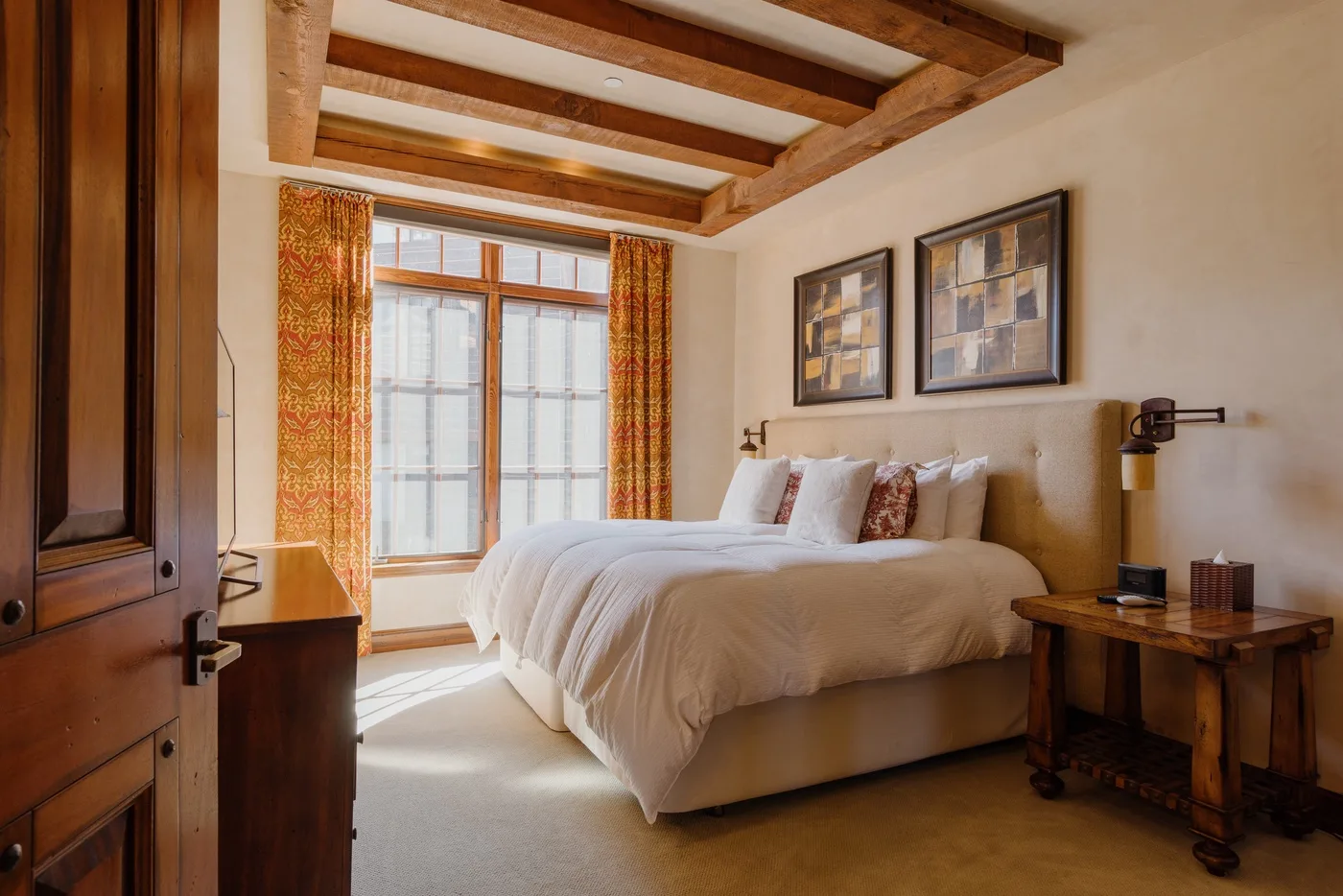 A bedroom with a large bed, framed artwork, and a bright window.