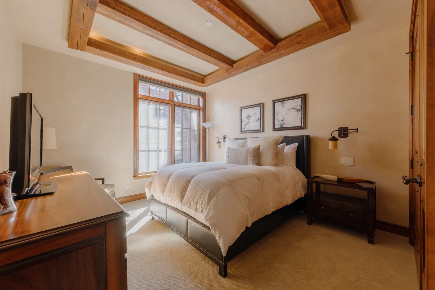 A bedroom with a large bed, a window, and exposed wooden ceiling beams.