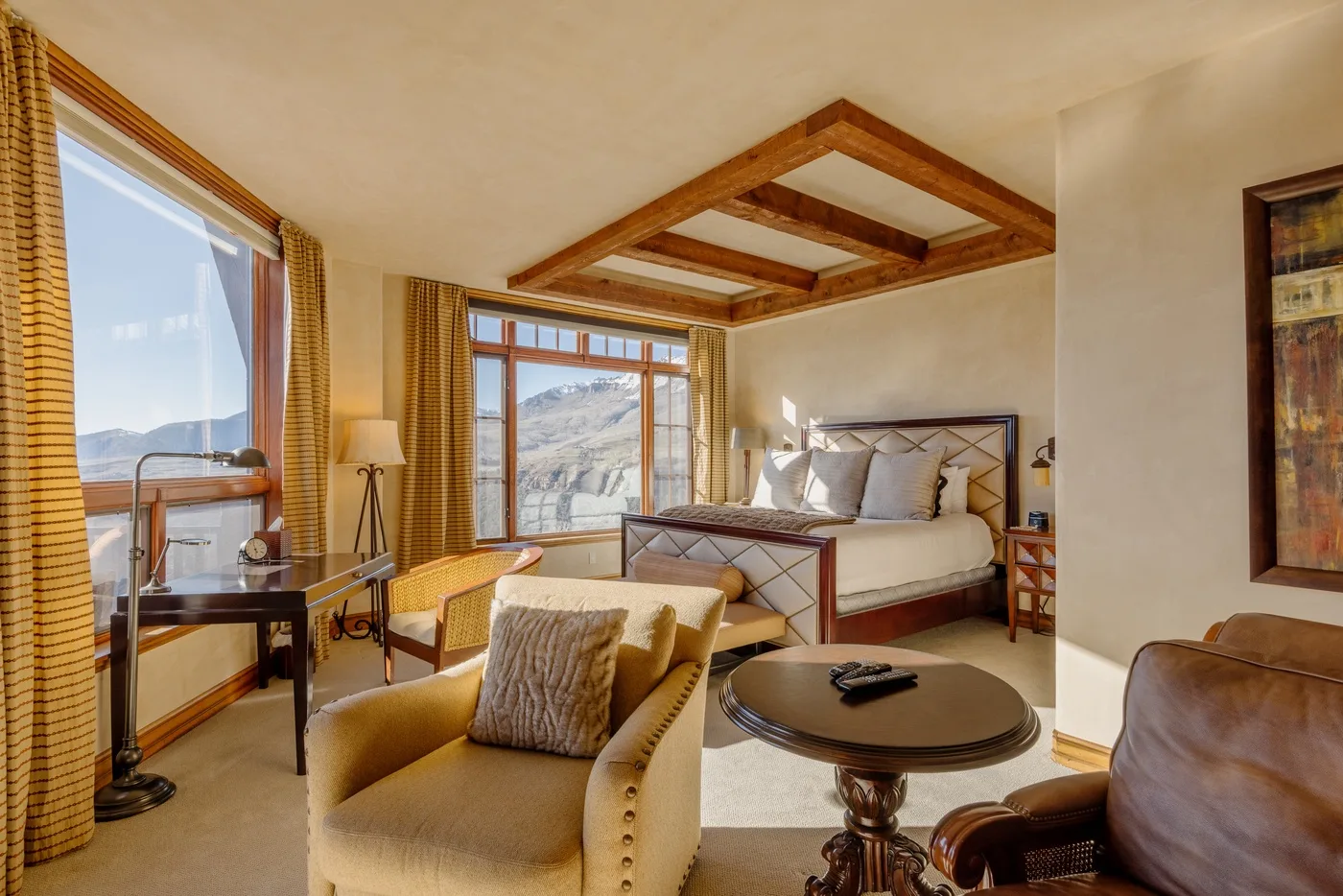 Un dormitorio con una cama grande, asientos y ventanas con vistas a un paisaje montañoso.