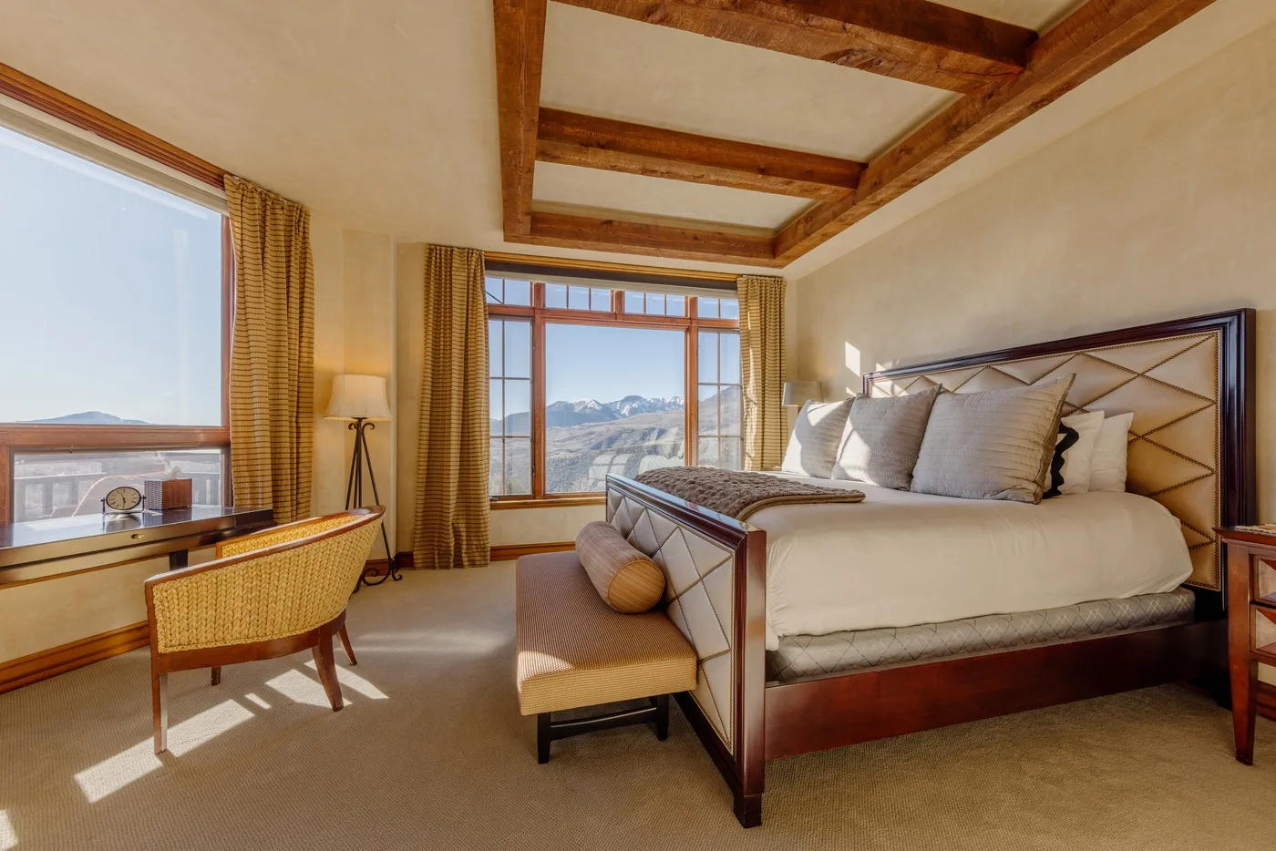 Un dormitorio con una cama grande, un banco y ventanas con vistas a un paisaje montañoso.