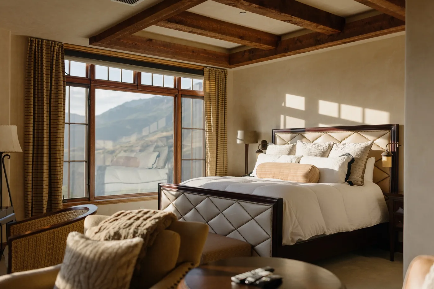 A bedroom with a large bed beside tall windows overlooking a mountain view.